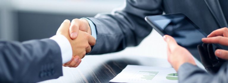 Handshake two guys give a handshake in a business environment as a greeting or a deal well done, a third person is using a tablet